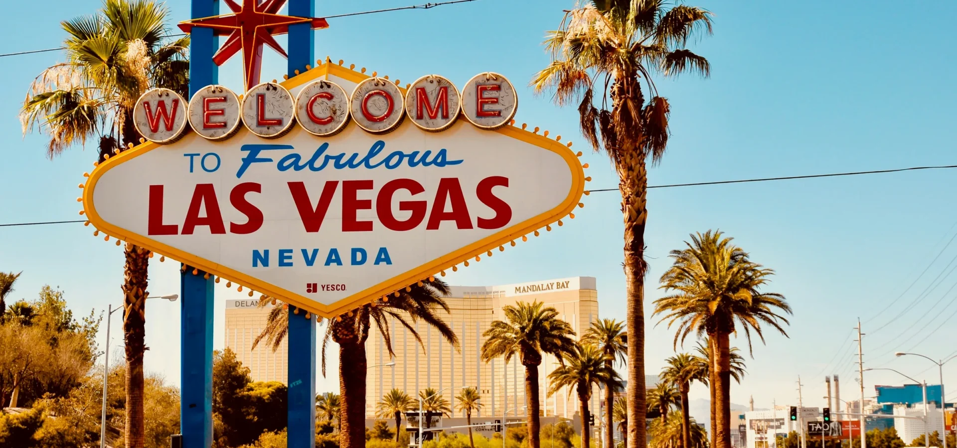 Iconic Welcome to Fabulous Las Vegas Nevada sign with palm trees and casinos in background under clear blue sky.